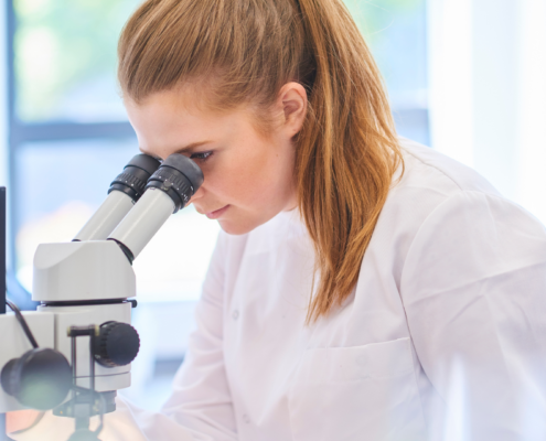 Žena v laboratóriu pozoruje vzorku cez mikroskop.
